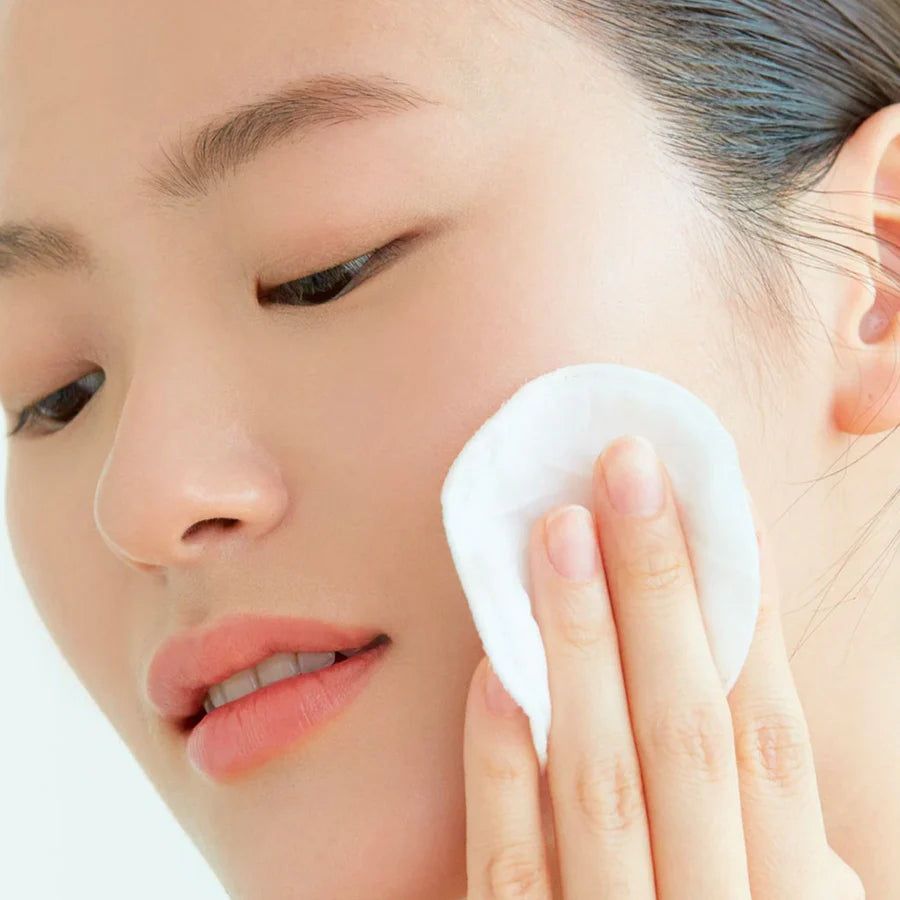 Woman gently applying AXIS-Y daily purifying toner on her face using a cotton pad