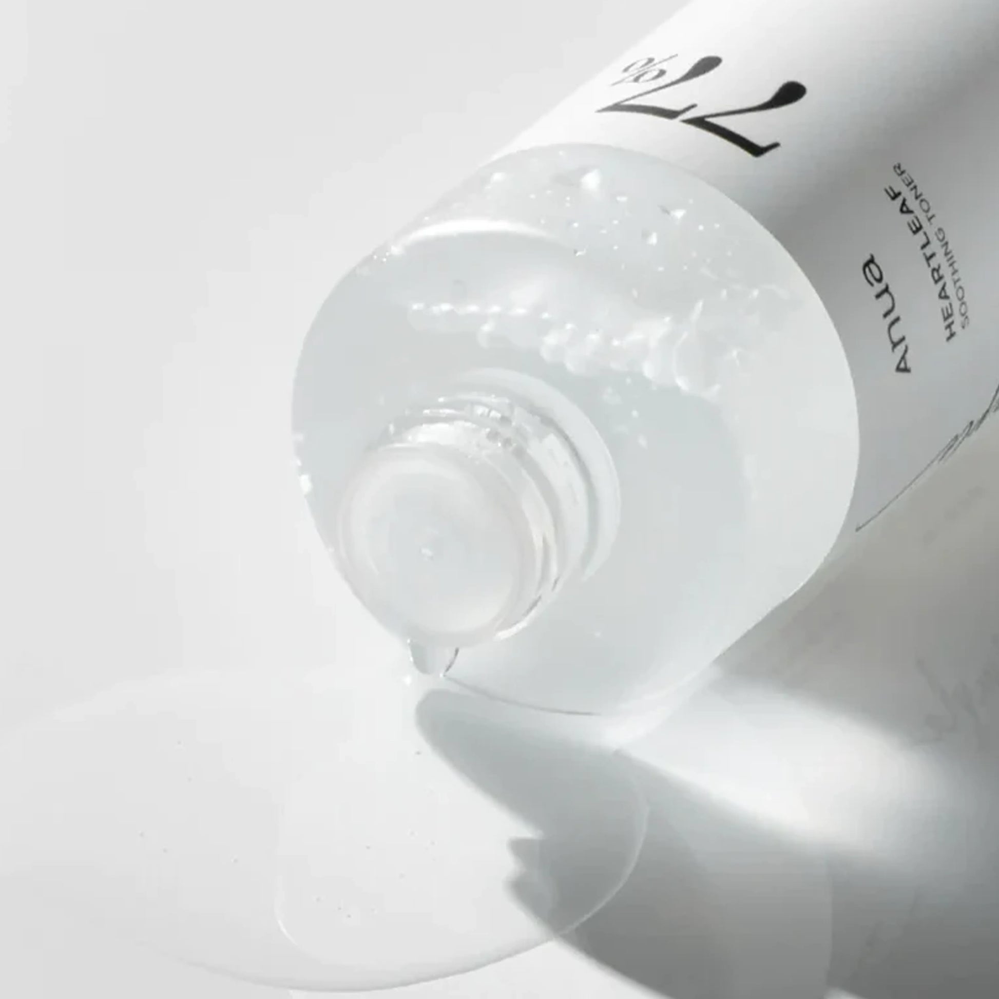 Anua Heartleaf 77 Soothing Toner mini bottle pouring clear toner liquid on white surface