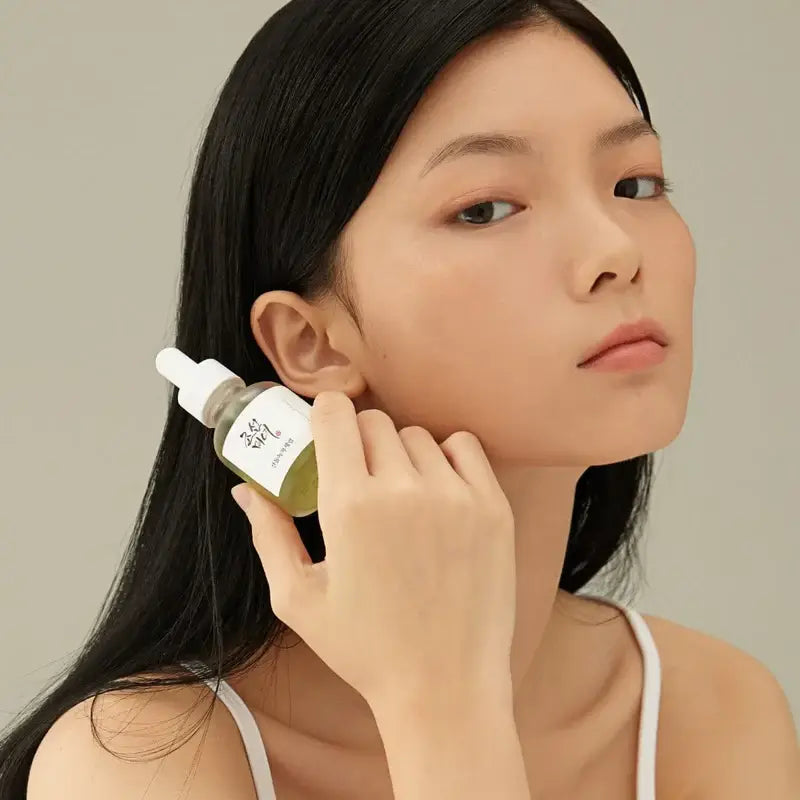Beauty Of Joseon Green Tea Calming Serum in a glass bottle held by a model for skincare routine